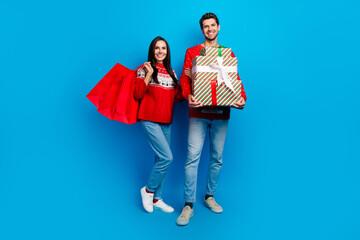 Sticker - Photo of two cheerful optimistic good mood people holding shopping bags presents on christmas eve isolated on blue color background