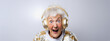 Excited elderly granny wearing gold headphones and sparkly festive holiday sweater listening to music for New Year's eve countdown celebration, amazed expression, gray background