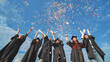 Happy graduates throwing up colorful confetti against the blue summer sky.