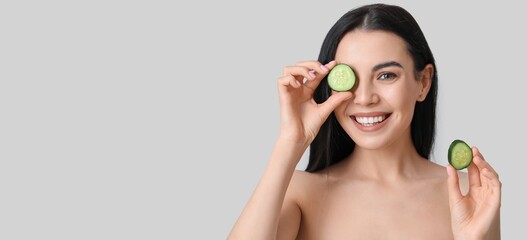 Poster - Beautiful young woman with cucumber slices on light background with space for text. Cosmetology concept