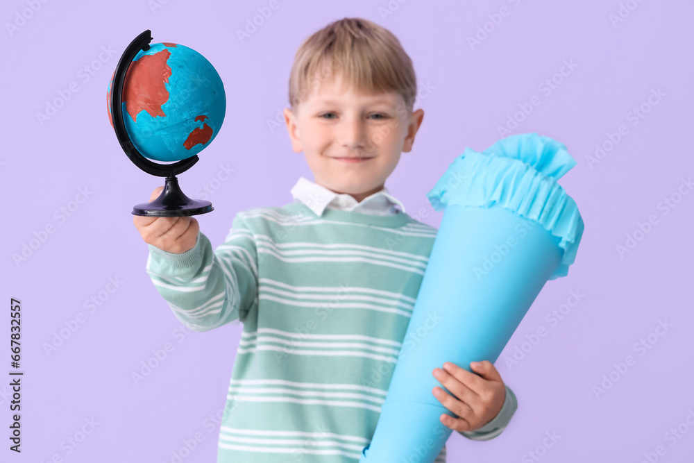 Happy little boy with blue school cone and globe on lilac background