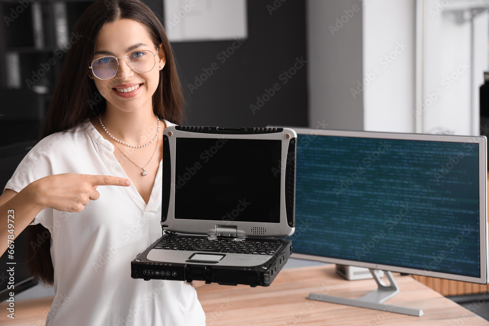 Pretty young female programmer pointing at blank screen of old laptop in office