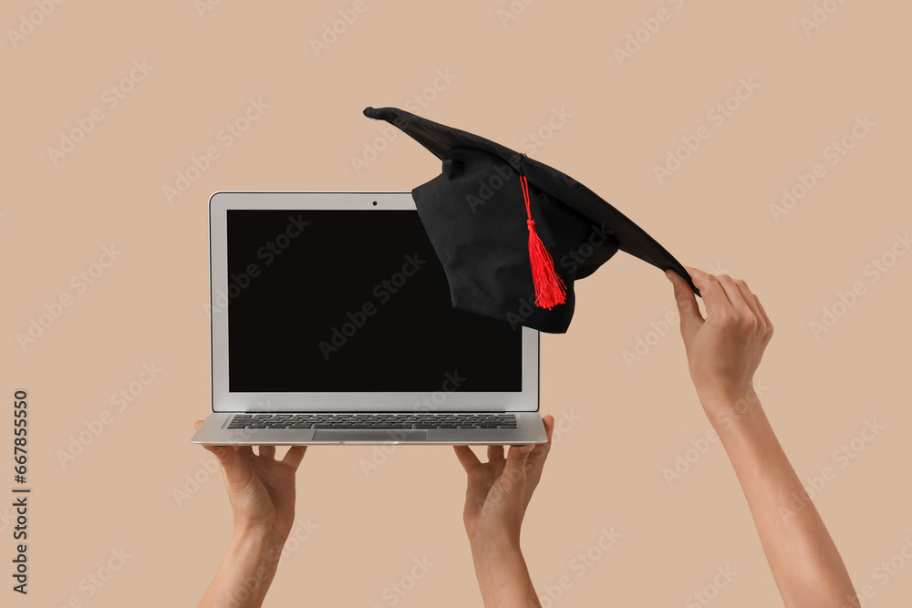 Women with blank laptop and graduation hat on beige background