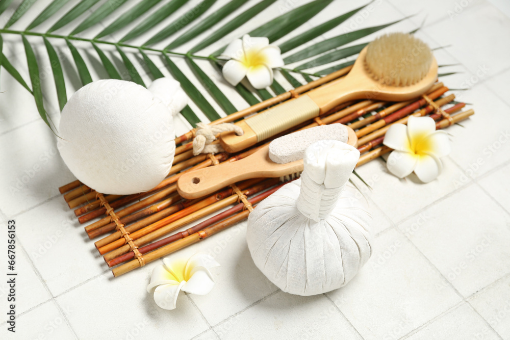 Composition with spa accessories, palm leaf and tropical flowers on light tile background