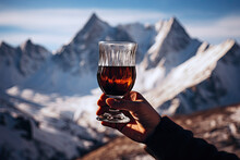 A Hand Holds A Glass Of Mulled Wine Or Hot Black Tea On Snowy Mountain Peaks Background.