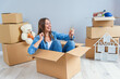 © gorynvd - Happy woman drinks champagne from a glass while sitting inside a cardboard box in new apartment.