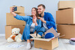 © gorynvd - Young couple taking selfies in their new home while sitting among cardboard boxes. Happy attractive young couple is moving, making a selfie, cuddling and smiling.