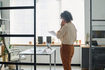 Poster - Back view of mature grey haired female chief executive officer with mobile phone by ear talking to applicant, business partner or subordinate