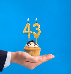 Hand delivering birthday cupcake - Candle number 43 on blue background