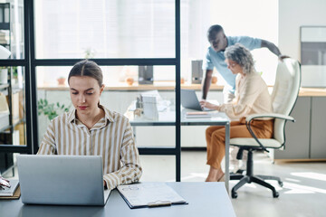 Aufkleber - Young secretary or analyst using laptop while sitting by desk with financial document with graphic data and looking through information on screen
