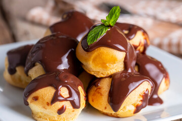 Wall Mural - Delicious profiteroles with chocolate and white plate. Selective focus image on light background.