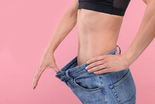 Slim Woman Wearing Big Jeans On Pink Background, Closeup. Weight Loss