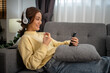 Asian woman sit on the sofa in the living room at home to enjoy their favorite songs.  girl wears headphones to listen to music, mood and hobby, modern wireless tech concept