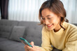 woman sitting on a sofa using a mobile phone, Happy relaxed smiling lady laughing holding smartphone, looking at cellphone enjoying doing online e-commerce shopping in mobile apps or watching videos.