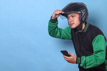 Asian man with helmet wear green jacket, holding smartphone and looking far away isolated on blue background with free space for ads. 