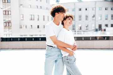 Young smiling beautiful woman and her handsome boyfriend in casual summer white t-shirt and jeans clothes. Happy cheerful family. Female having fun. Couple posing in street at sunny day