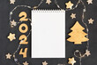 Horizontal dark gray textured background with note pad, wooden numbers 2024 garland and Christmas tree. Template for design with copy space in rustic crafts style.