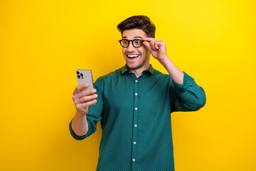 Photo of funky cheerful man wear green stylish clothes hold glasses read social media post coment isolated on yellow color background