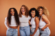 © Flamingo Images - Diverse women in jeans and white tops laughing against an orange background