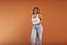 Woman Wearing A Tank Top And Jeans Laughing On An Orange Background