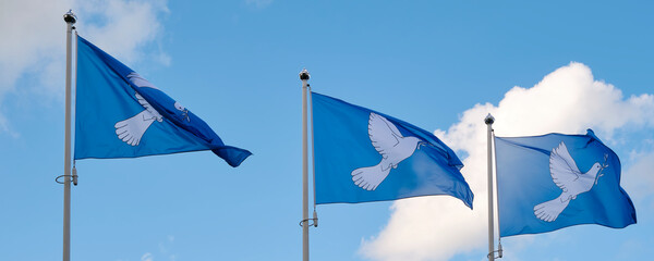 Three blue peace flags in a row printed with a dove with an olive branch in its beak. The dove with the branche is the international symbol of peace. Panorama image.