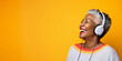 Studio portrait of mature black woman listening on headphones and laughing, yellow background	
