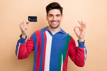 Sticker - Portrait of cheerful guy beaming smile arm hold debit card demonstrate okey symbol isolated on beige color background