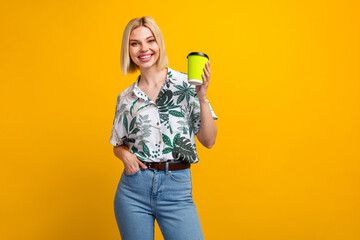 Sticker - Photo portrait of lovely young lady hold paper cup coffee tea dressed stylish leaves print garment isolated on yellow color background