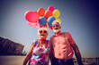 Outdoor portrait of a happy elderly couple with sunglasses wearing colorful shirts holding balloons