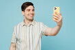 © ViDi Studio - Young happy man he wears striped shirt casual clothes doing selfie shot on mobile cell phone post photo on social network isolated on plain pastel light blue cyan background studio. Lifestyle concept.