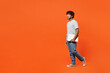 Full body side view young happy IT Indian man he wearing t-shirt casual clothes hold closed laptop pc computer walking going isolated on orange red color background studio portrait. Lifestyle concept.
