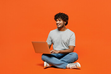 Wall Mural - Full body young smiling happy IT Indian man wears t-shirt casual clothes sit hold use work on laptop pc computer type message isolated on orange red color background studio portrait Lifestyle concept
