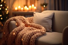 Gray sofa with warm knitted plaid and pillows. Burning aroma candles with Christmas or New Year decor on background. Cozy home concept. Autumn or winter atmosphere. Still life details of living room