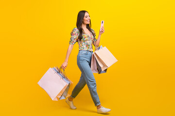 Poster - Full length photo of intelligent girl hold new outfit look at smartphone go shopping to empty space isolated on yellow color background