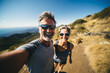 A happy middle-aged couple with sunglasses doing a selfie while hiking in the mountains in summer.