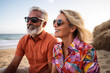Portrait of a happy middle-aged couple with sunglasses wearing colorful shirts sitting on a beach.