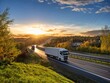Trucks driving on the highway winding through forested landscape in autumn colors at sunset