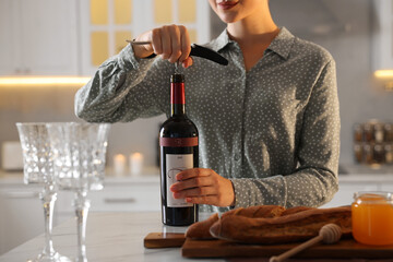 Canvas Print - Romantic dinner. Woman opening wine bottle with corkscrew at table in kitchen, closeup