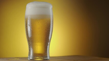 Canvas Print - Glass of beer rotates slowly on a yellow background, there is condensation on the beer glass and there are a lot of bubbles and foam inside. A great beer background for your projects.