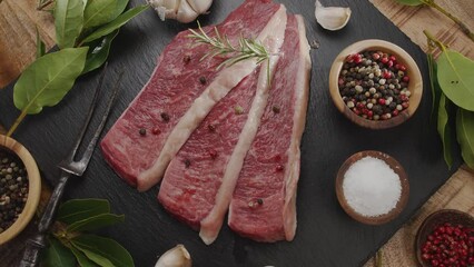 Poster - Three sliced pieces of picanha beef with spices and herbs on a gray stone countertop slowly rotate in the frame. Traditional Portuguese food.