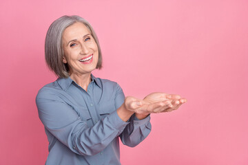 Sticker - Photo of grateful kind retired woman dressed blue stylish shirt plams demonstrating product empty space isolated on pink background