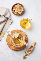 Wall Mural - Chamomile herbal tea with lemon in a glass cup and teapot with flowers on a light background. The concept of a healthy drink for health and sleep.