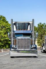 Front of the bonnet classic big rig semi truck tractor with chrome accessories and tall exhaust pipes and refrigerated semi trailer parked on the rest area taking break for truck driver rest