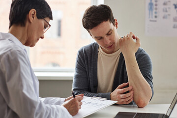 Wall Mural - Portrait of young man showing skin rash to doctor during consultation in dermatology clinic