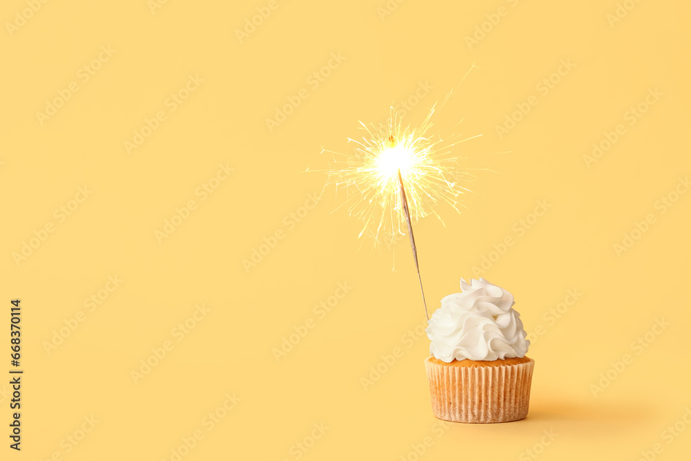 Tasty birthday cupcake with sparkler on orange background