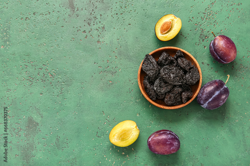 Bowl with tasty dried plums on green background