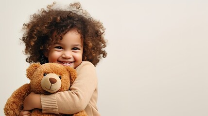 Wall Mural - portrait of little curly smiling kid girl hugging teddy bear on white background with copy space. toddler embracing her toy bear