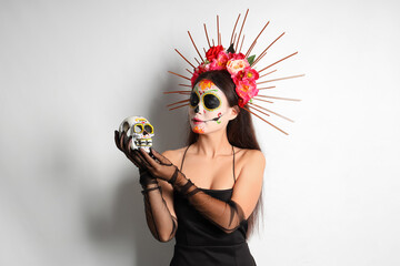 Poster - Young woman with painted skull on light background. Mexico's Day of the Dead (El Dia de Muertos) celebration