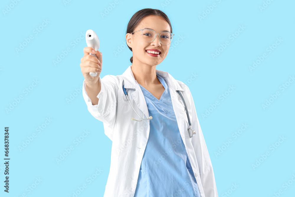 Female Asian doctor with infrared thermometer on blue background