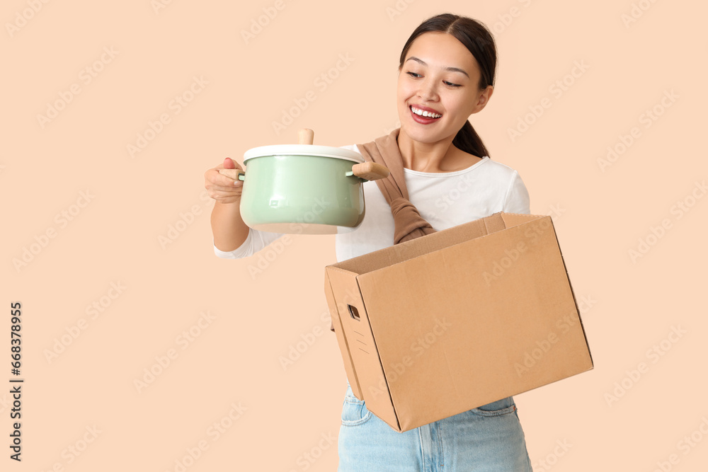 Young Asian woman with cooking pot and parcel box on beige background